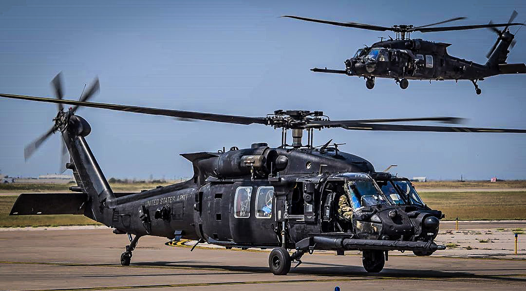 Two US Army MH-60 Black Hawks, one taxiing and one hovering behind it