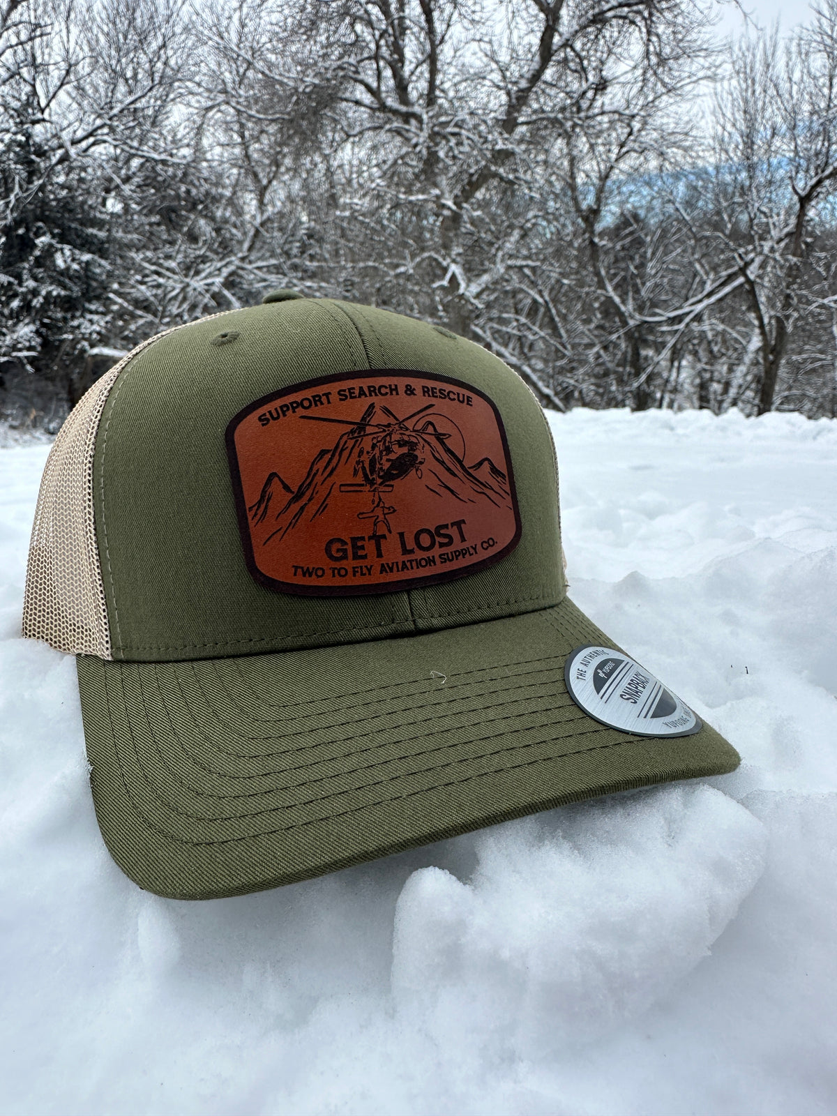 Get Lost V2 olive green and tan trucker cap with leather Support Search & Rescue patch, photographed in snow